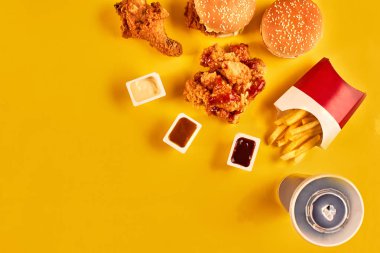 Fast food yemek üstten görünüm. Patates kızartması, hamburger, Sarı zemin üzerine mayonez, ketçap soslar.