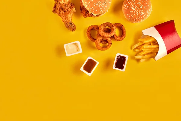 快餐菜顶视图。法式炸薯条，汉堡，沙拉酱和番茄酱的酱汁，在黄色背景上. — 图库照片