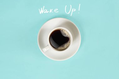 Fincan sade kahve ve üzerinde mavi arka plan izole Wake Up yazı Üstten Görünüm