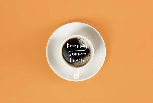 Widok góry filiżankę czarnej kawy i utrzymując kawy świeże literowanie na białym tle na pomarańczowym tle — Zdjęcie stockowe