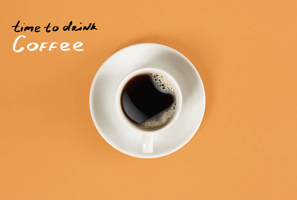 Top view of cup of black coffee and "Time to drink Coffee" lettering isolated on orange background