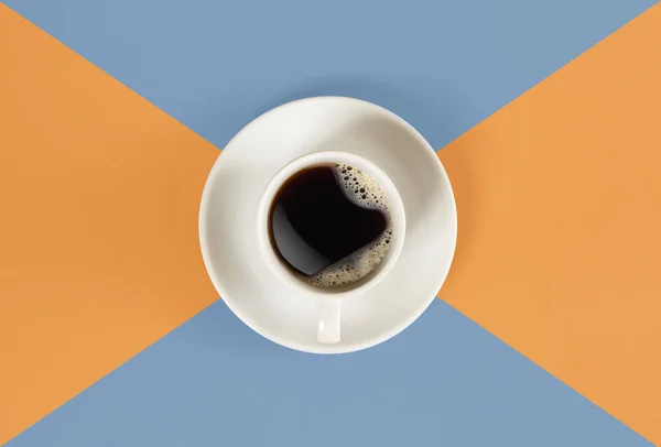 Una taza de café negro sobre fondo naranja y azul. Vista desde arriba . — Foto de Stock