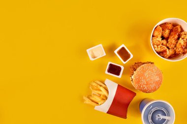 Fast food yemek üstten görünüm. Patates kızartması, hamburger, Sarı zemin üzerine mayonez, ketçap soslar.
