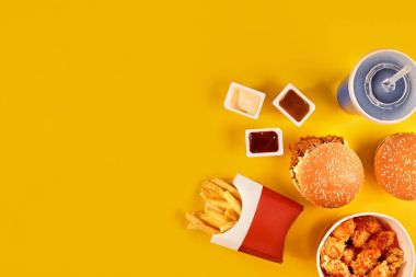 Fast food yemek üstten görünüm. Patates kızartması, hamburger, Sarı zemin üzerine mayonez, ketçap soslar.