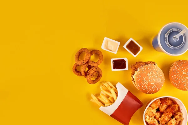 Fast food dish top view. French fries, hamburger, mayonnaise and ketchup sauces on yellow background.