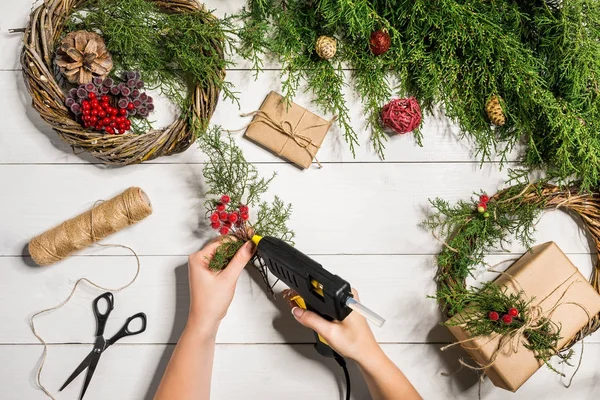 Natal feito à mão fundo diy. Fazendo grinalda xmas artesanato e ornamentos. Vista superior da mesa de madeira branca com as mãos femininas . — Fotografia de Stock