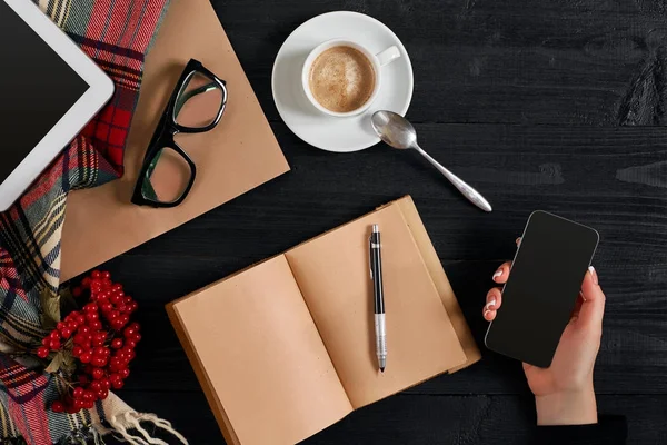 Жінки тримають телефон з чорним екраном над столом з чашкою кави, ноутбука і планшета — стокове фото