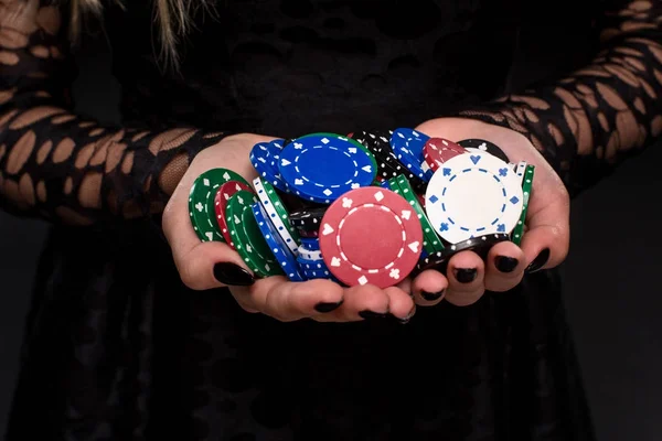 Elegant female casino player holding a handful of chips on black background, hands close up