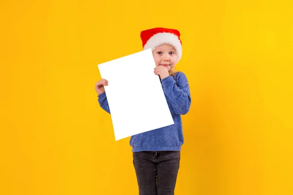 Cute little girl in Santa Claus hat with a white blank paper sheet. Christmas, x-mas, New Year, Winter, people, advertisement, sale concept. — Stock Photo, Image