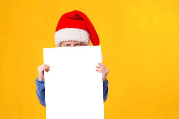 Cute little girl in Santa Claus hat with a white blank paper sheet. Christmas, x-mas, New Year, Winter, people, advertisement, sale concept. Royalty Free Stock Photos