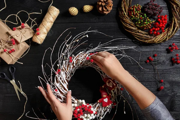Visão superior de mãos femininas fazer uma grinalda de Natal. Presentes e pergaminhos embalados, ramos de abeto e ferramentas em mesa de madeira . — Fotografia de Stock