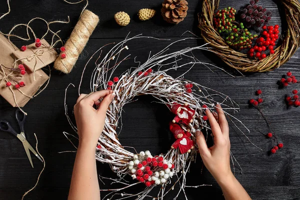 Visão superior de mãos femininas fazer uma grinalda de Natal. Presentes e pergaminhos embalados, ramos de abeto e ferramentas em mesa de madeira . — Fotografia de Stock