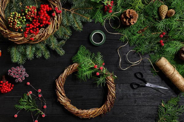 Faça uma coroa de Natal com suas próprias mãos. Ramo de abeto, grinalda de Natal e presentes em um fundo de madeira preta — Fotografia de Stock
