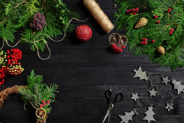 Faça uma coroa de Natal com suas próprias mãos. Ramo de abeto, grinalda de Natal e presentes em um fundo de madeira preta — Fotografia de Stock