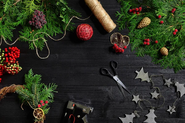 Faça uma coroa de Natal com suas próprias mãos. Ramo de abeto, grinalda de Natal e presentes em um fundo de madeira preta — Fotografia de Stock