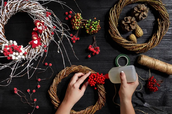 Visão superior de mãos femininas fazer uma grinalda de Natal. Presentes e pergaminhos embalados, ramos de abeto e ferramentas em mesa de madeira . — Fotografia de Stock