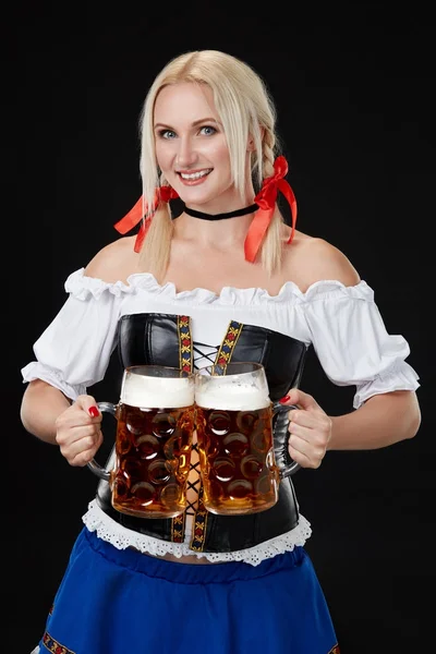 Jonge sexy vrouw draagt een dirndl met twee bier mokken op zwarte achtergrond — Stockfoto