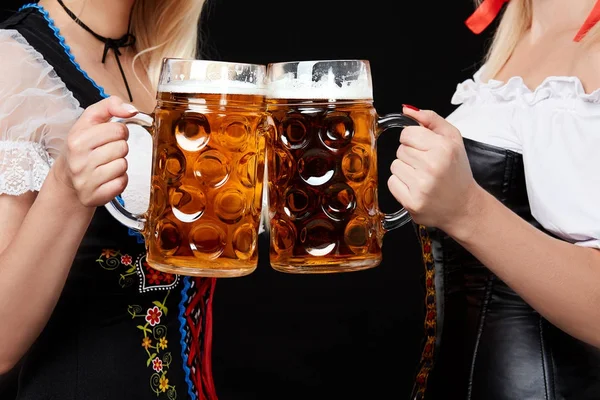 Jóvenes y hermosas chicas bavarianas con dos tazas de cerveza sobre fondo negro — Foto de Stock
