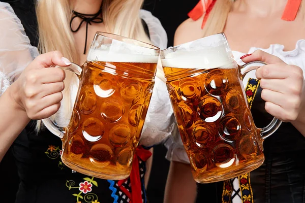 Junge und schöne bayrische Mädchen mit zwei Bierkrügen auf schwarzem Hintergrund — Stockfoto