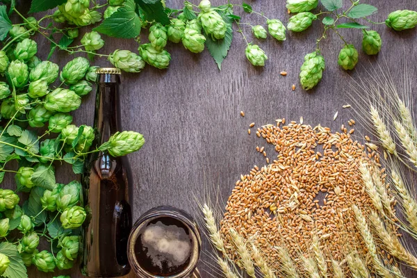 Cerveza de botella y vidrio con trigo y lúpulo como ingredientes de elaboración de cerveza en la vista superior y área de espacio de copia — Foto de Stock