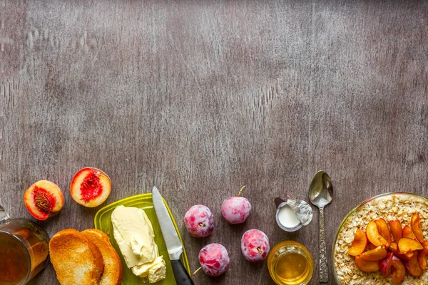 Harina de avena con ciruelas y melocotón, tostadas con mantequilla y miel sobre una mesa de madera. El concepto de un desayuno saludable — Foto de Stock