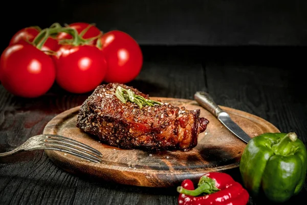 Filete a la parrilla sazonado con especias y hierbas frescas servidas en una tabla de madera con tomate fresco y pimientos rojos y verdes — Foto de Stock