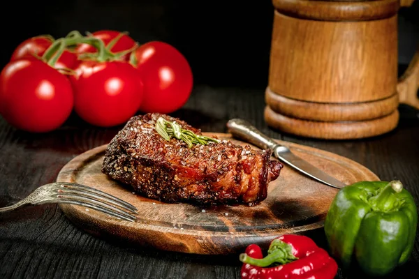 Bife grelhado temperado com especiarias e ervas frescas servido em uma tábua de madeira com caneca de madeira de cerveja, tomate fresco, pimentão vermelho e verde — Fotografia de Stock