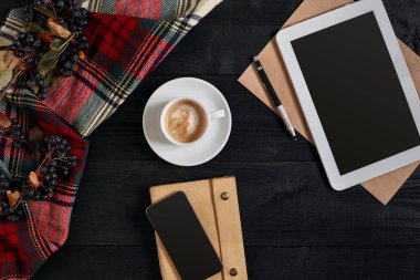 Görünümü akıllı telefon, tablet, eşarp bir kafes içinde gözlük ile defter ve latte siyah ahşap arka plan üzerine kahve fincan.