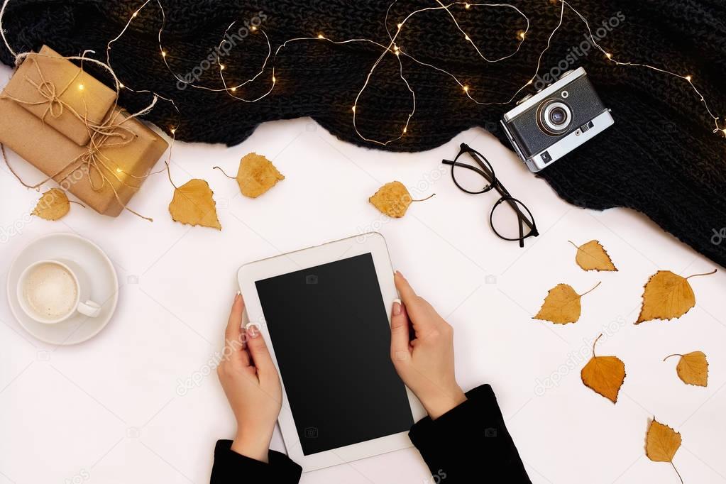 Top view,close-up of tablet computer with blank screen in hands of woman dressed in knitted sweater. Nearby is cup of coffee and scarf