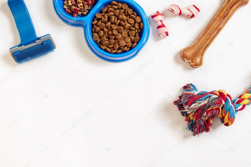 Dog care items, isolated on white background. Dry pet food in bowl, toy and bones. Top view