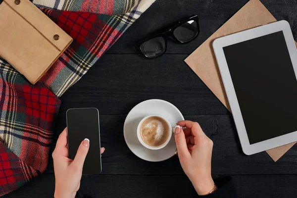 Жінки тримають телефон з чорним екраном над столом з чашкою кави і планшетом — стокове фото
