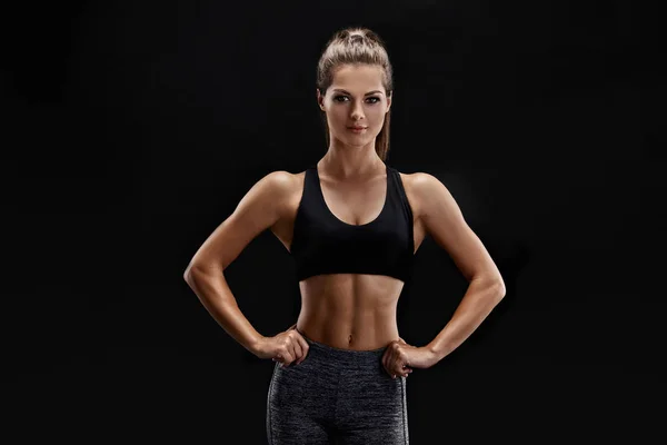 Foto de una mujer fuerte con abdomen muscular en ropa deportiva. Fitness modelo femenino posando sobre fondo negro . — Foto de Stock