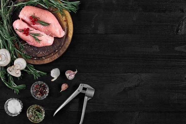 Raw chicken breast fillets on wooden cutting board with herbs, spices and mushrooms. Top view with copy space
