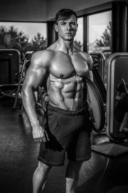 Yakışıklı ve kaslı bir adam, spor salonunda kameraya poz veriyor.