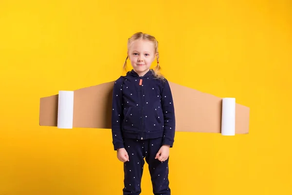 Маленька дівчинка носить саморобні картонні літаючі крила, прикидаючись пілотом для ремесла, уяви або концепції дослідження . — стокове фото