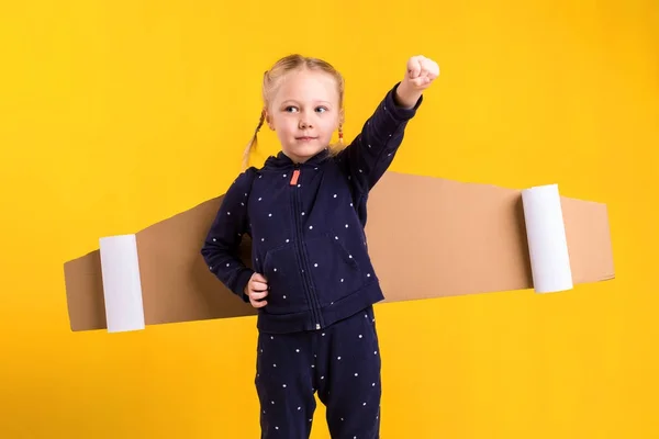 En liten jente har på seg flygende vinger av hjemmelaget papp, later som om hun er pilot for et håndverk, fantasi eller et utforskingskonsept . – stockfoto