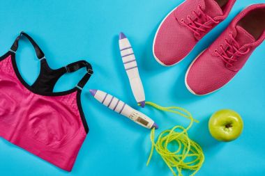 Düz kadın spor ekipmanları pembe renkte ile ip atlama ve spor ayakkabılar mavi arka plan üzerinde göklere