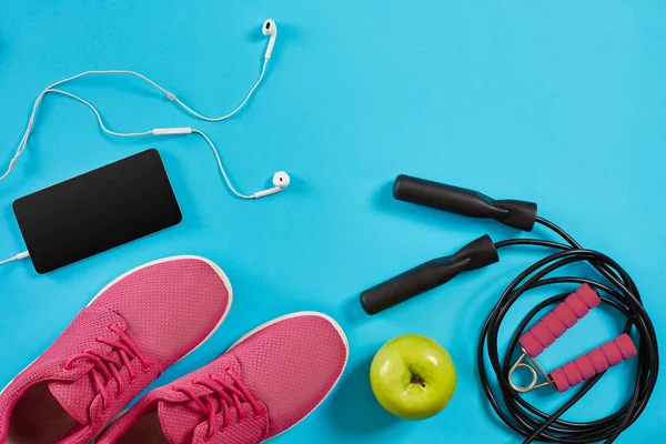 Flat lay shot of sneakers, jumping rope, dumbbells and smartphone on blue background.