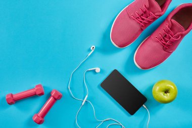 Düz Spor donatımı atış yatıyordu. Spor ayakkabı, halter, kulaklık, telefon mavi zemin üzerine.
