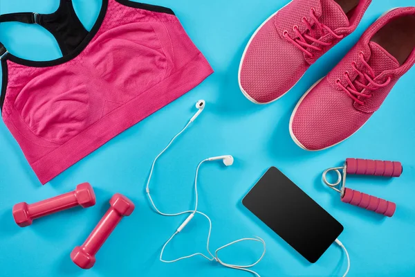 Plan plat de l'équipement sportif. Baskets, haltères, écouteurs et téléphone sur fond bleu . — Photo