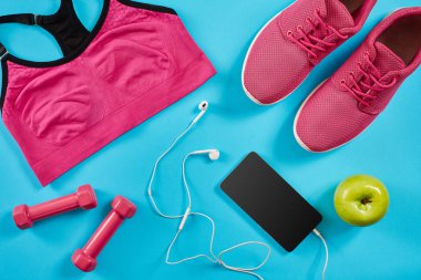 Düz Spor donatımı atış yatıyordu. Spor ayakkabı, halter, kulaklık, telefon mavi zemin üzerine.