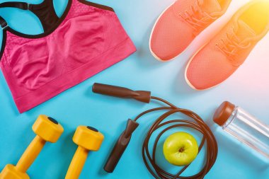 Sporcu kadın giyim, halter ve şişe suyu üzerinde parlak mavi arka plan ile ayarlayın. Güneş parlaması