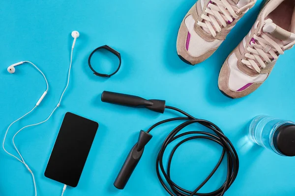 Flachschuss von Sportgeräten. Turnschuhe, Springseil, Kopfhörer und Telefon auf blauem Hintergrund. — Stockfoto