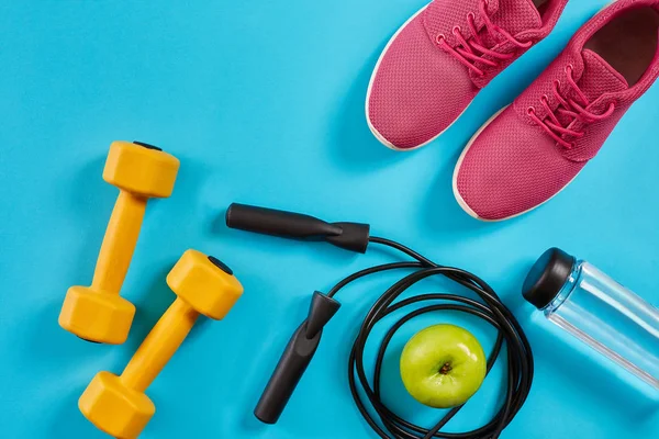 Düz yatıyordu kadın spor ekipmanları, ip atlama, şişe su ve pembe ayakkabı mavi zemin üzerine