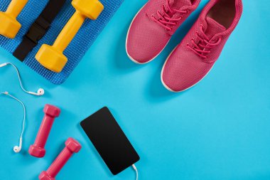 Spor ayakkabı, halter ve mavi arka plan üstünde hareket eden telefon. Üstten Görünüm. Fitness, spor ve sağlıklı yaşam konsepti.