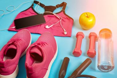 Sporcu kadın giyim, halter ve şişe suyu üzerinde parlak mavi arka plan ile ayarlayın. Güneş parlaması