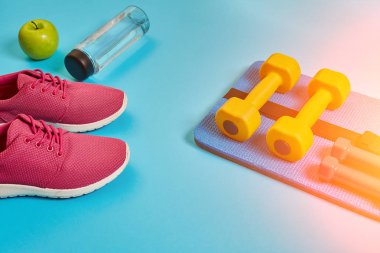 Sağlıklı kavramı, spor ayakkabı ve bir şişe su ve dumbell ile diyet planı mavi arka plan, sağlıklı yiyecek ve egzersiz kavramı. Güneş parlaması