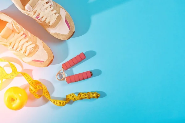Sneakers with measuring tape on cyan blue background. Centimeter in yellow color near white trainers, close up. Sun flare — Stock Photo, Image