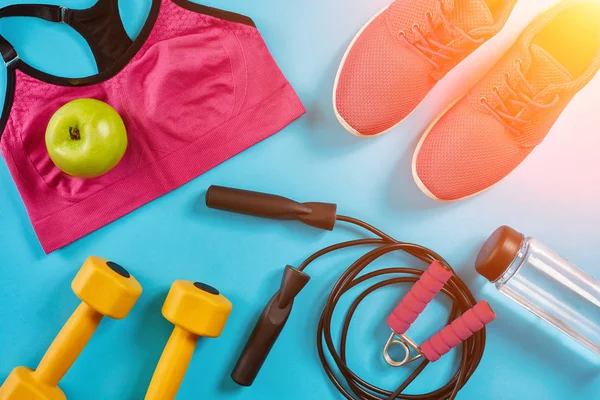 Sporcu kadın giyim, halter ve şişe suyu üzerinde parlak mavi arka plan ile ayarlayın. Güneş parlaması