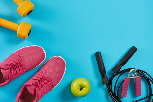 Flat lay de equipamentos esportivos femininos, corda de salto, halteres e tênis rosa no fundo azul — Fotografia de Stock